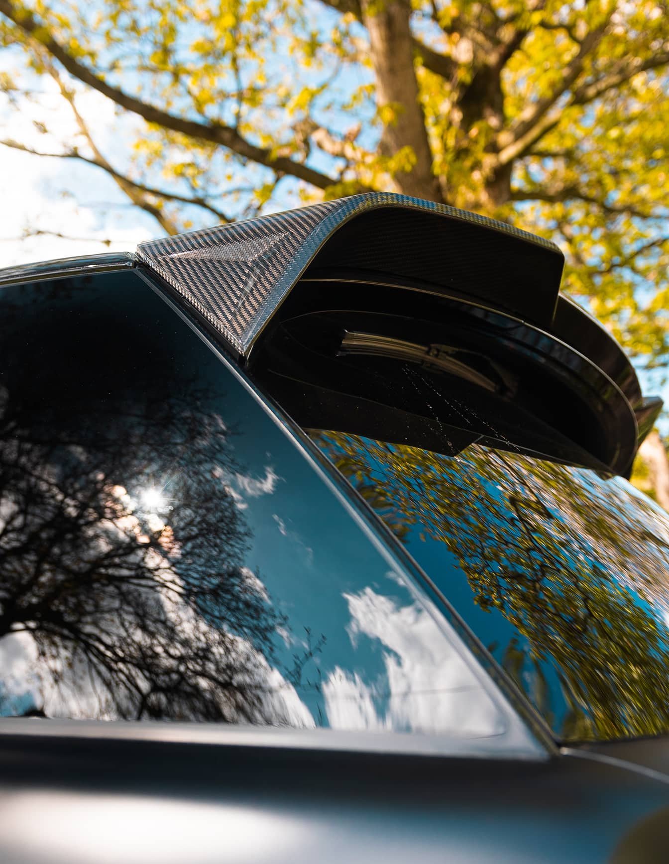 A custom Forge Land Rover Range Rover with a carbon fiber spoiler, reflecting a bright sky and green trees.