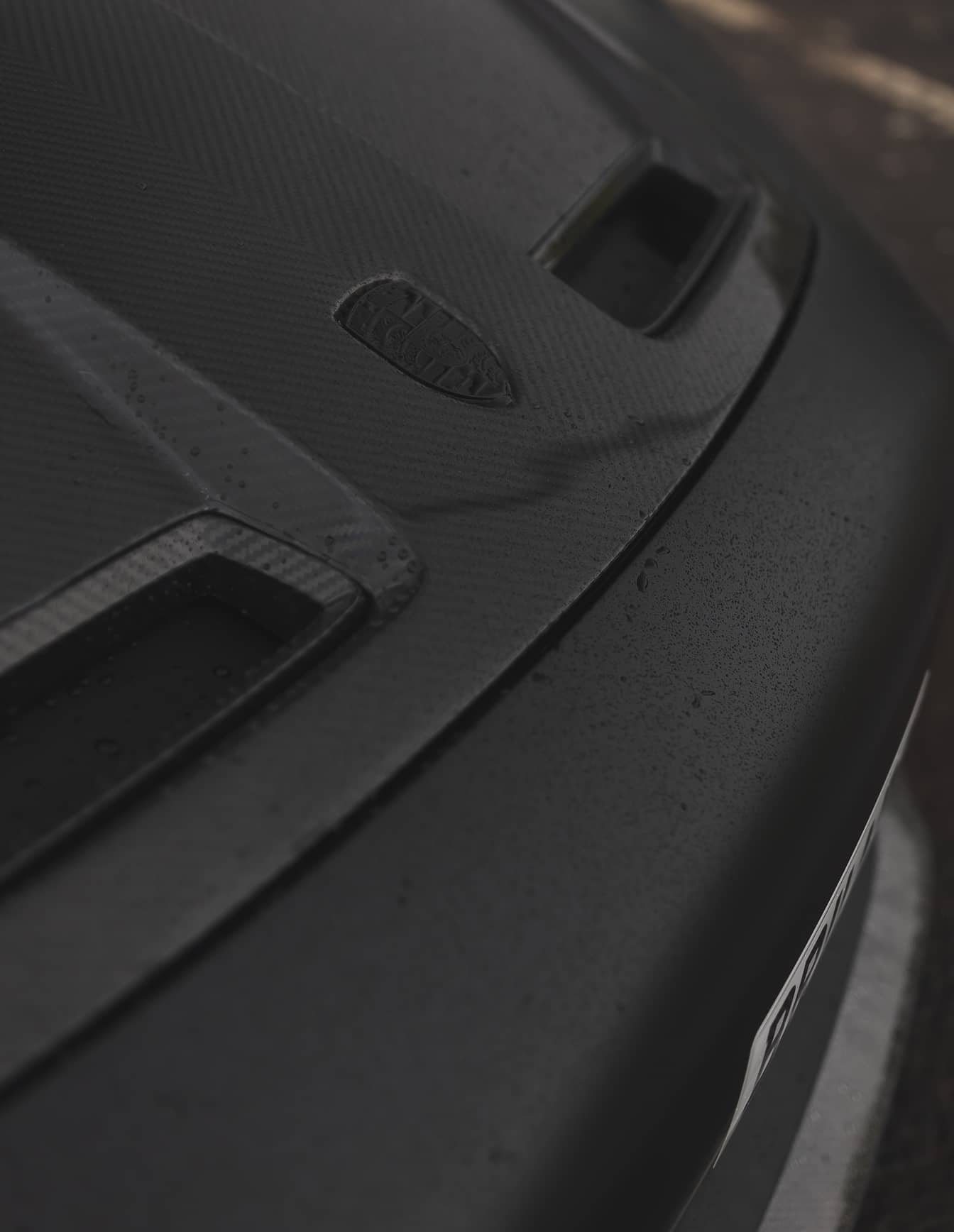A custom Forge Porsche 911 Carrera Turbo with a carbon fiber hood and vents, lightly covered in raindrops, parked on a wet surface.