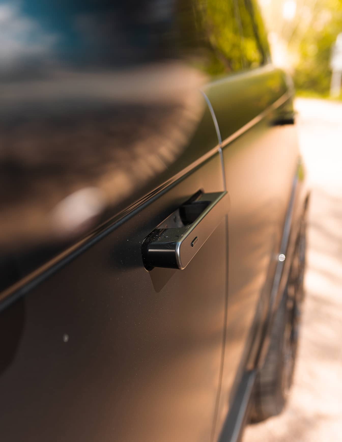 A custom Forge Land Rover Range Rover's matte black door and flush handle are seen up close, with a blurred natural background.