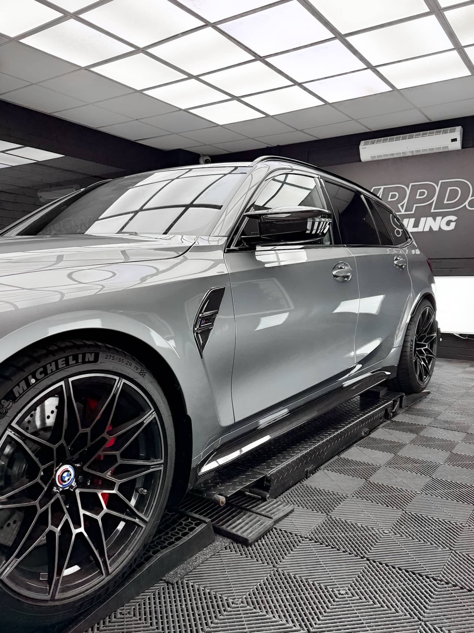 A custom Forge BMW M5 Touring sits elevated on a mechanic lift inside a bright detailing workshop.