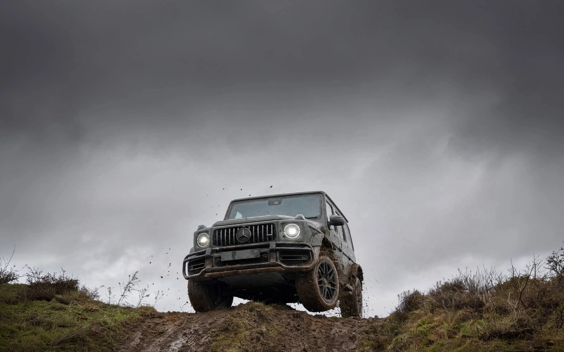 A custom Forge Mercedes G63 covered in mud drives over an earthy hill beneath an overcast sky.