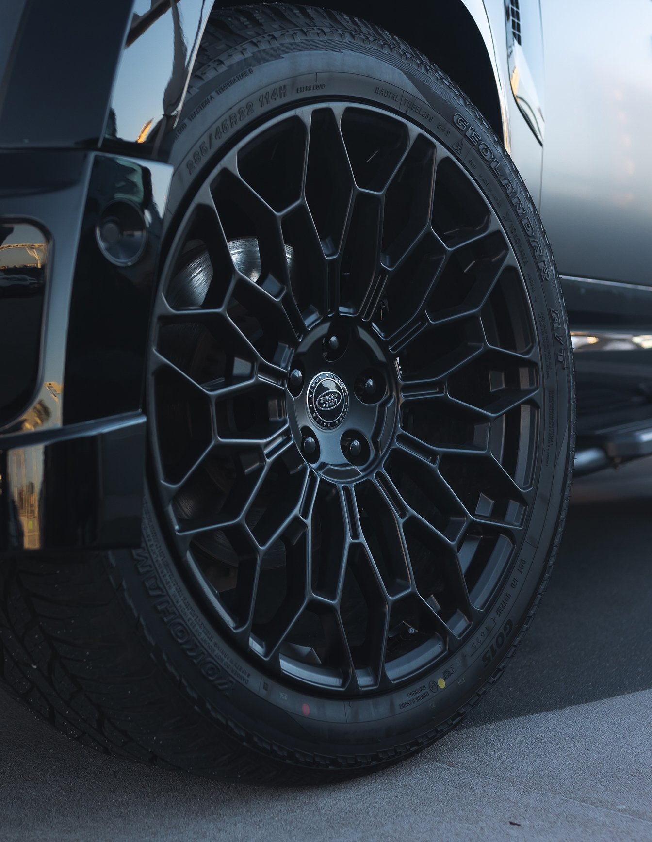 A custom Forge Land Rover Defender 130 wheel with a black geometric spoke design and a Yokohama tire is parked on asphalt.