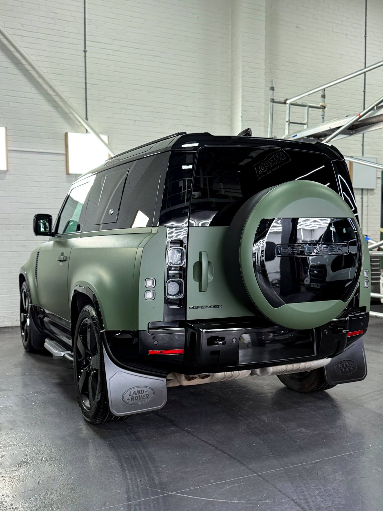 A custom Forge Land Rover Defender 90 with a matte green finish is parked inside a brightly lit workshop.