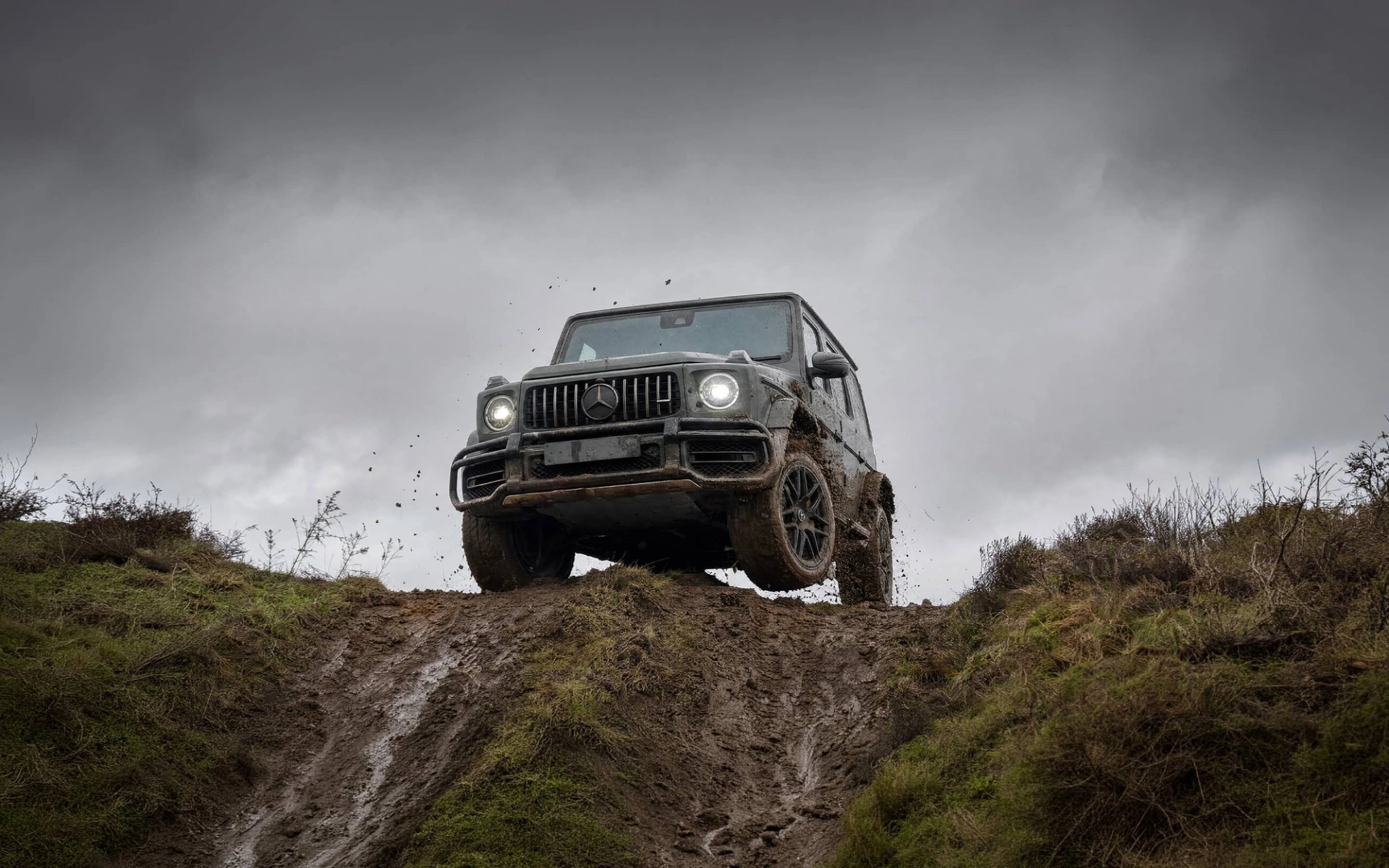 A custom Forge Mercedes G63 navigates a steep, muddy incline beneath an overcast sky.