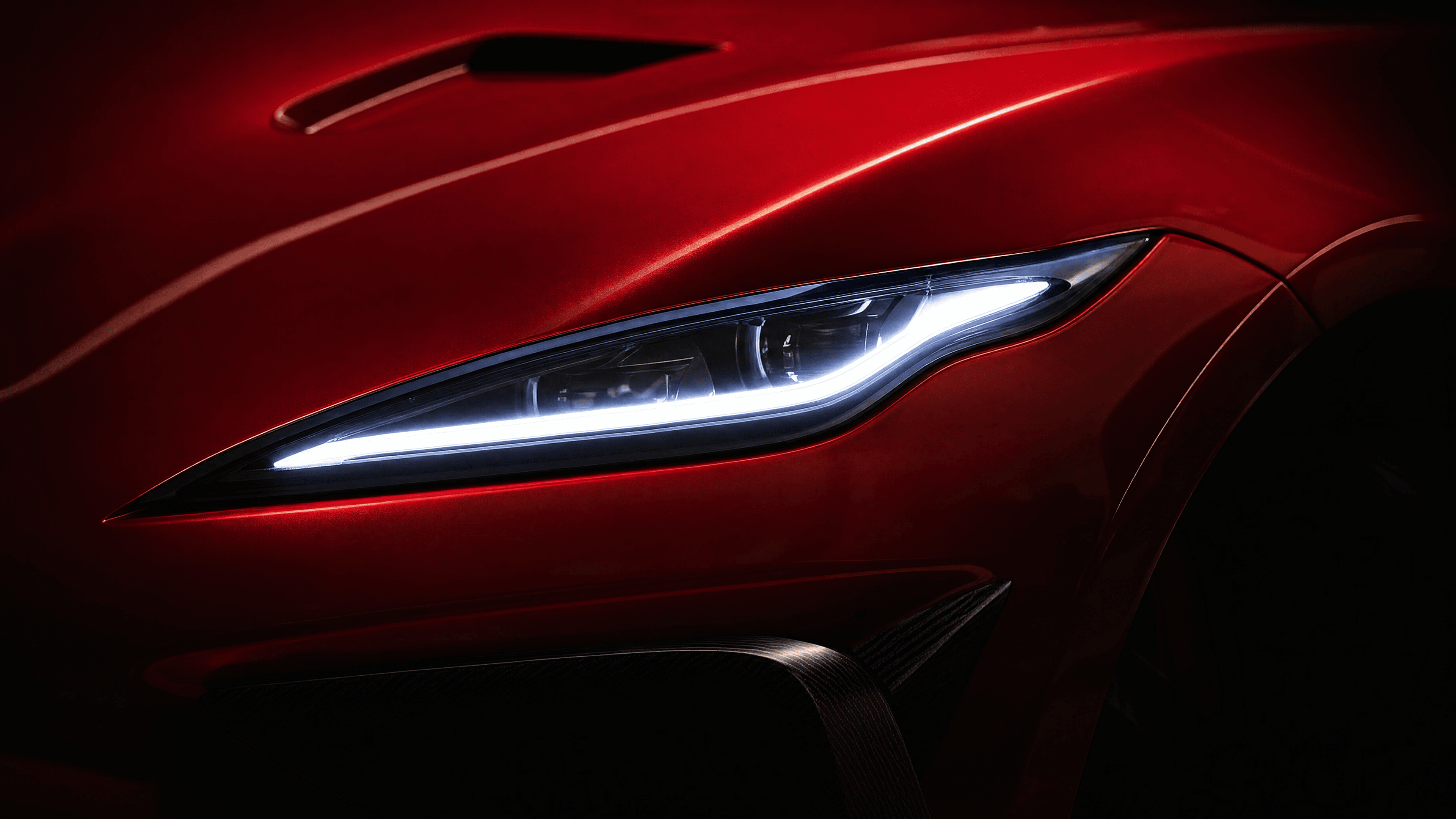 A close-up of a custom Forge vehicle's red hood, with a bright LED headlight and a carbon fiber vent visible in a dark setting.