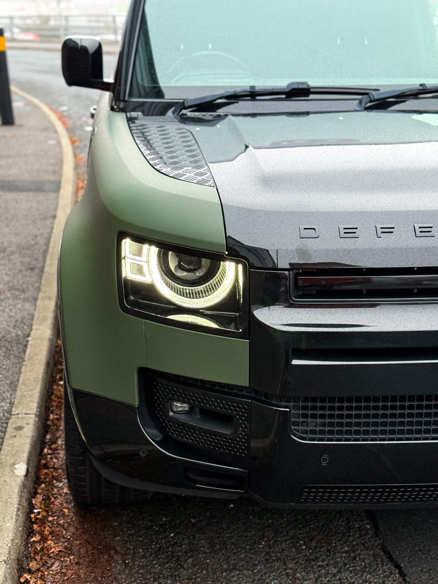 A close-up of a custom Forge Land Rover Defender 90 parked on a roadside with its headlights illuminated.