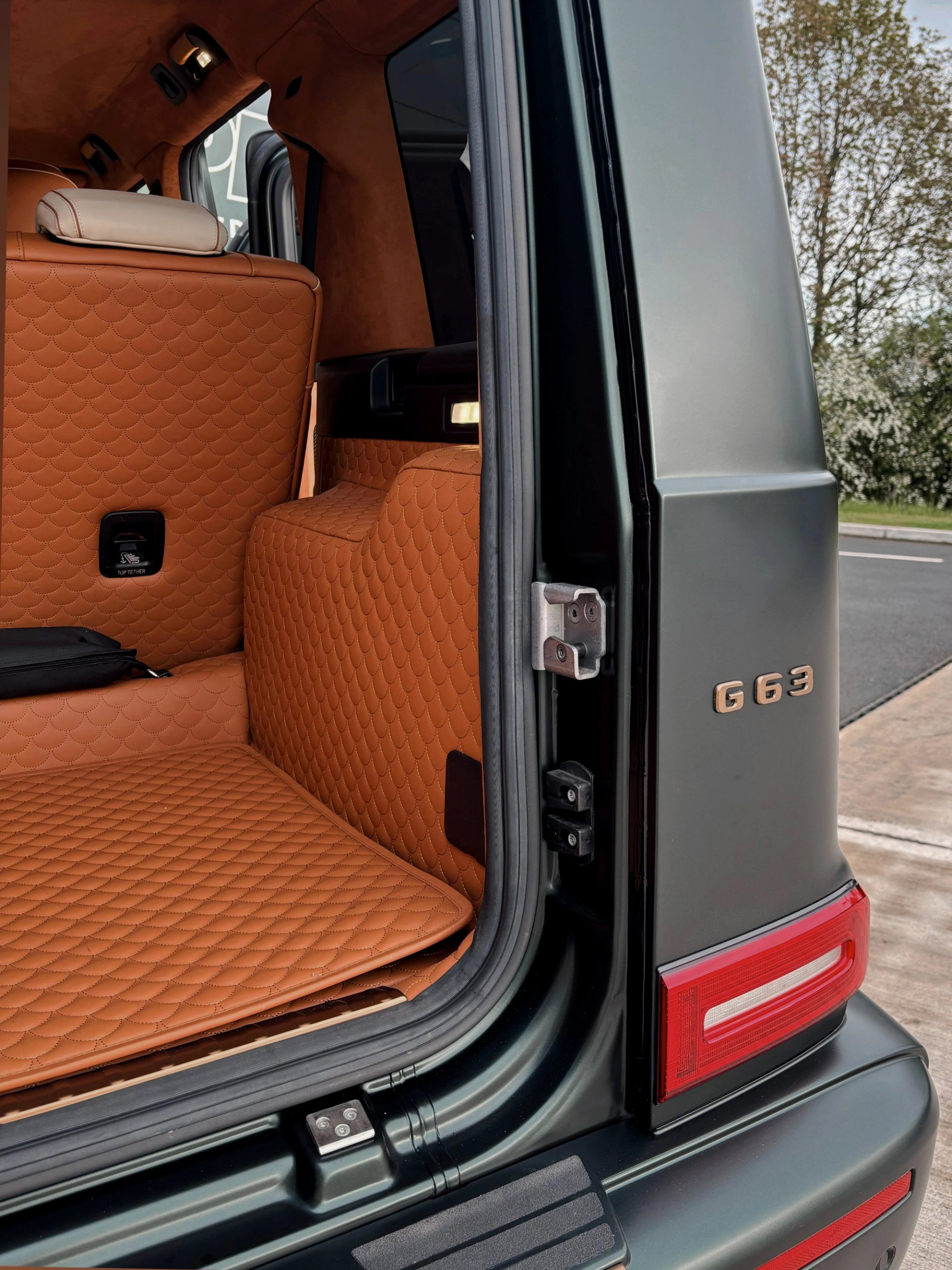 An open rear door of a custom Forge Mercedes G63 reveals diamond-quilted tan leather interior lining and trim.