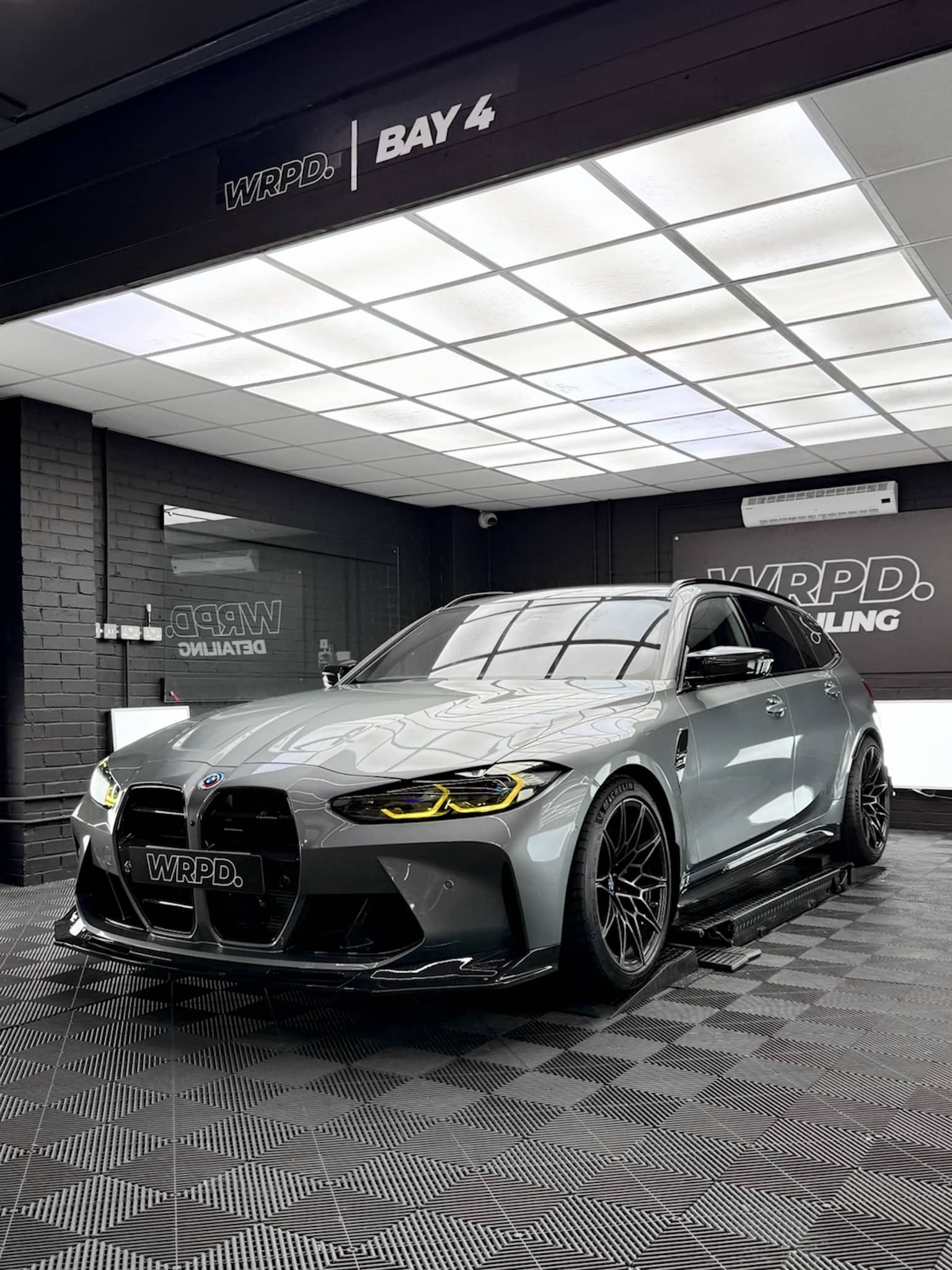 A custom Forge BMW M5 Touring sits parked on lifts inside a brightly lit detailing workshop.