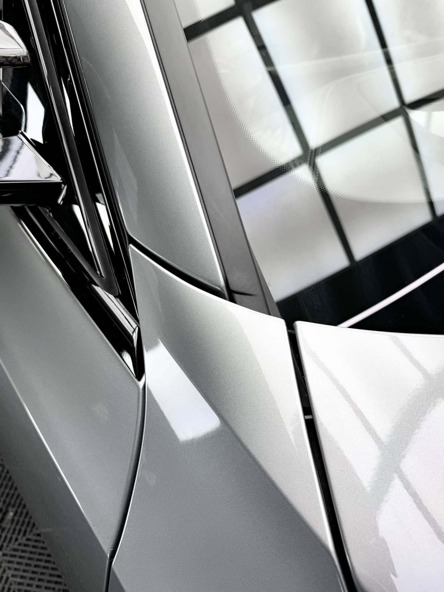 Close-up of the grey exterior body panels and A-pillar on a custom Forge BMW M5 Touring parked inside a brightly lit showroom.