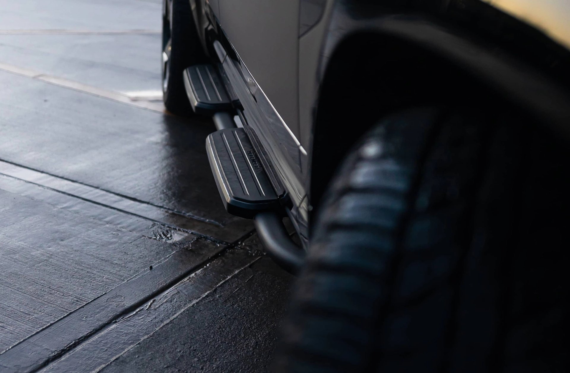 A custom Forge Land Rover Defender 110's running boards and tire are visible on a wet, dark paved surface.