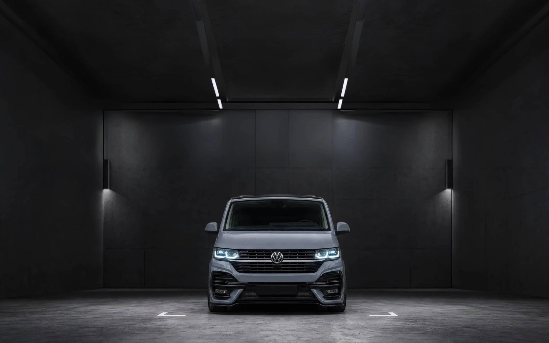 A custom Forge Volkswagen T6.1, painted gray, is parked head-on in a dark, minimalist garage with bright overhead strip lighting.