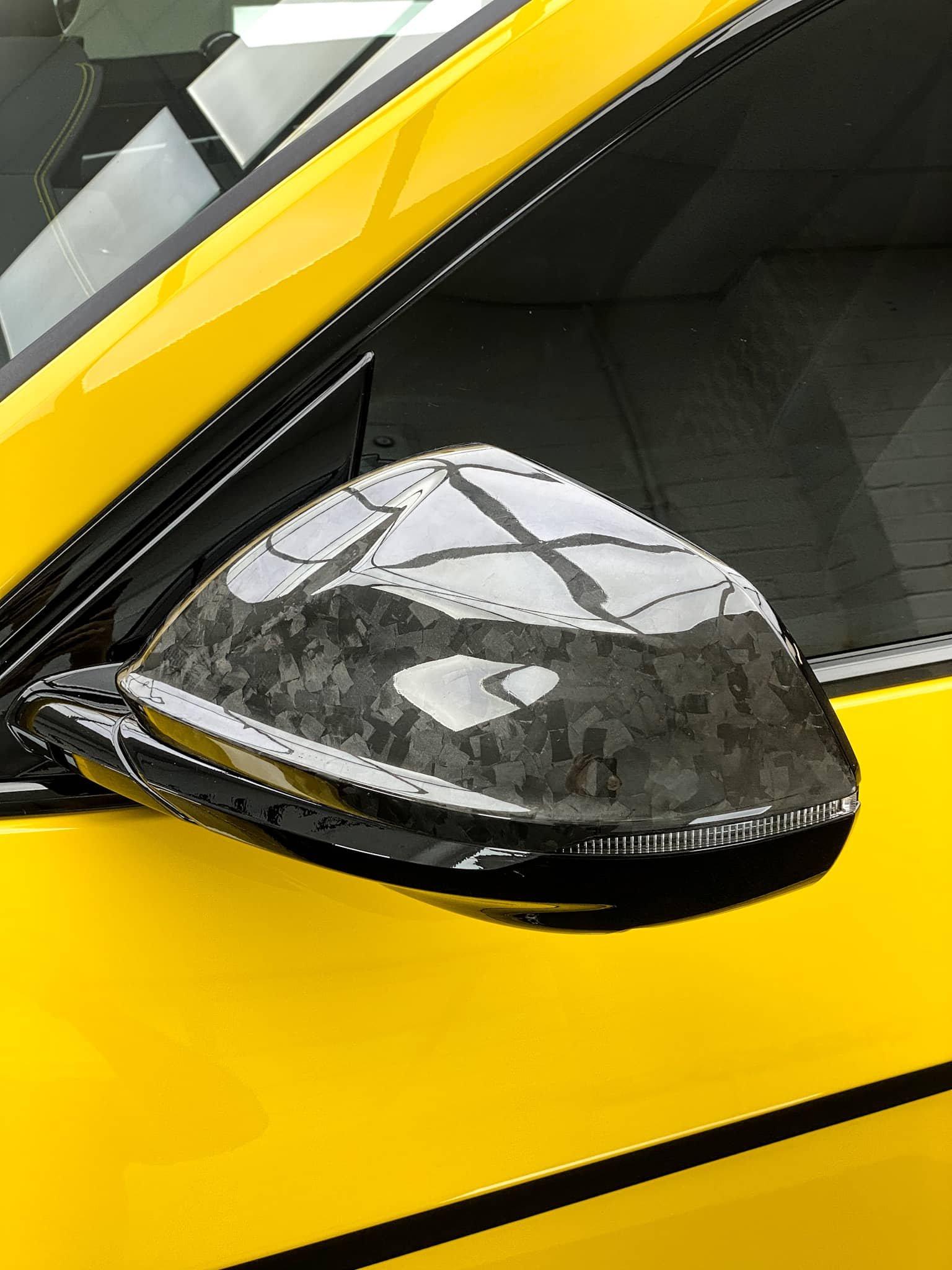 A custom Forge Lamborghini Urus features a forged carbon fiber side mirror cap against its bright yellow bodywork.