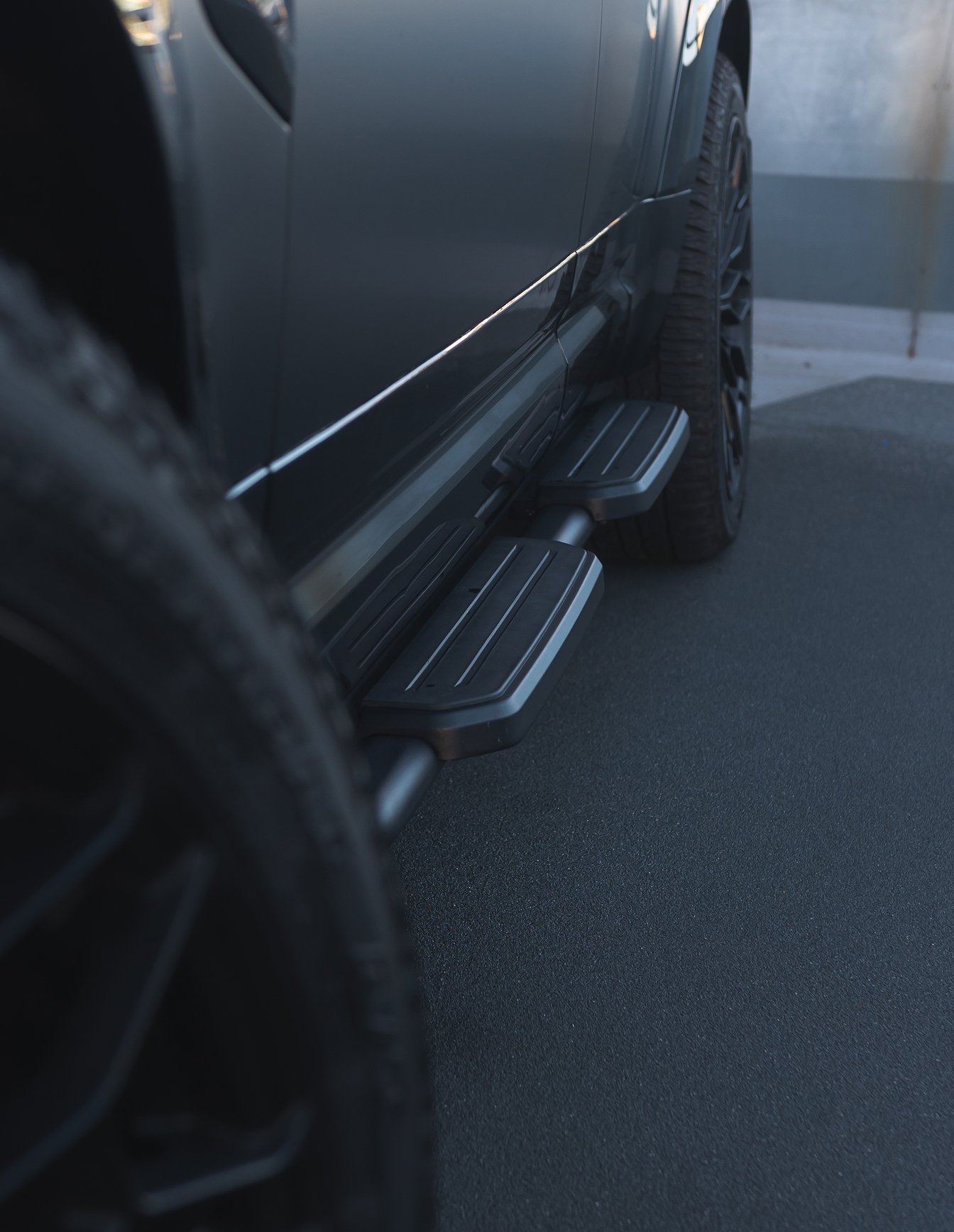 A custom Forge Land Rover Defender 130's black running boards and tire are visible from a low angle on a dark, textured surface.